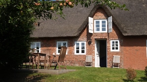 Ein Backsteinhaus mit einem Reetdach, ein Holztisch mit Stühlen und ein kleiner Garten.