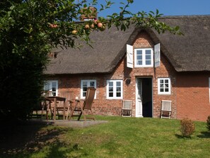 A brick house with a thatched roof, a wooden table with chairs, and a small garden. - Ferienhaus auf der kleinen Gaarde  – sauna, washing machine, garden, fireplace (Ockholm)