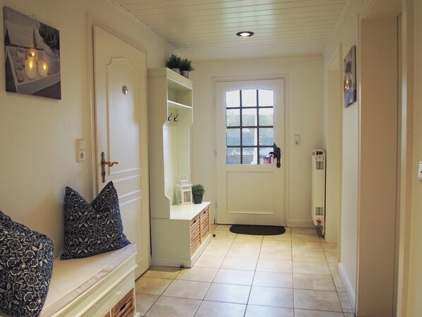 A hallway with a white door, a bench with cushions, a small table with a plant, and a window with a view of buildings outside.