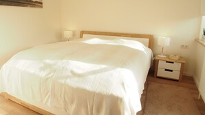 Une chambre à coucher comprenant un lit, des tables de chevet, une commode, une lampe, une prise de courant fixée au mur et un tableau accroché au mur.