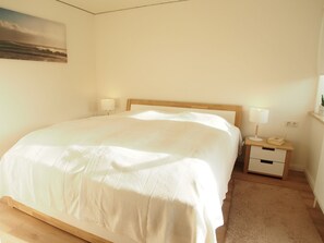 Ein Schlafzimmer mit Bett, Nachttischen, einer Lampe, einer Wandsteckdose und einem Bild an der Wand.