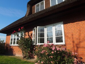A two-story house with a brick facade, white-framed windows, and a thatched roof.