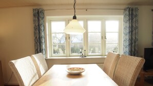 Un coin repas avec une table en bois, des chaises en osier, un luminaire suspendu et une fenêtre avec des rideaux.