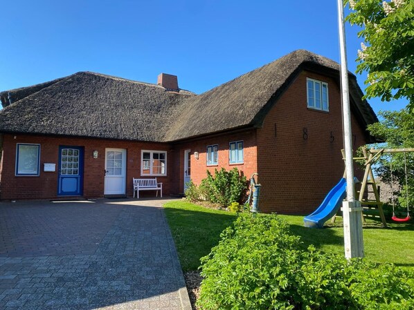 A red brick building with a thatched roof, a white door, and a blue window.