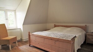 Een slaapkamer met een houten bed, een rieten stoel en een radiator.