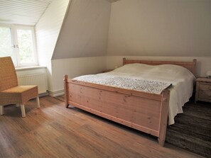 Ein Schlafzimmer mit einem hölzernen Bett, einem Korbsessel und einer Heizung.