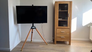 Een kamer met een flatscreen televisie op een statief, een houten kast met lades, en een radiator aan de muur.