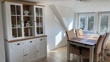 Ein Essbereich mit einem weißen Schrank, Korbstühlen und einem Tisch.
