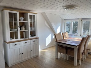 Ein Essbereich mit einem weißen Schrank, Korbstühlen und einem Tisch.