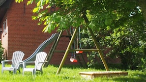 A brick building with a swing set and Adirondack chairs in a grassy area. - Wattwurm – shared Washing machine, use of garden, 2 floors, barbecue, parking (Ockholm)