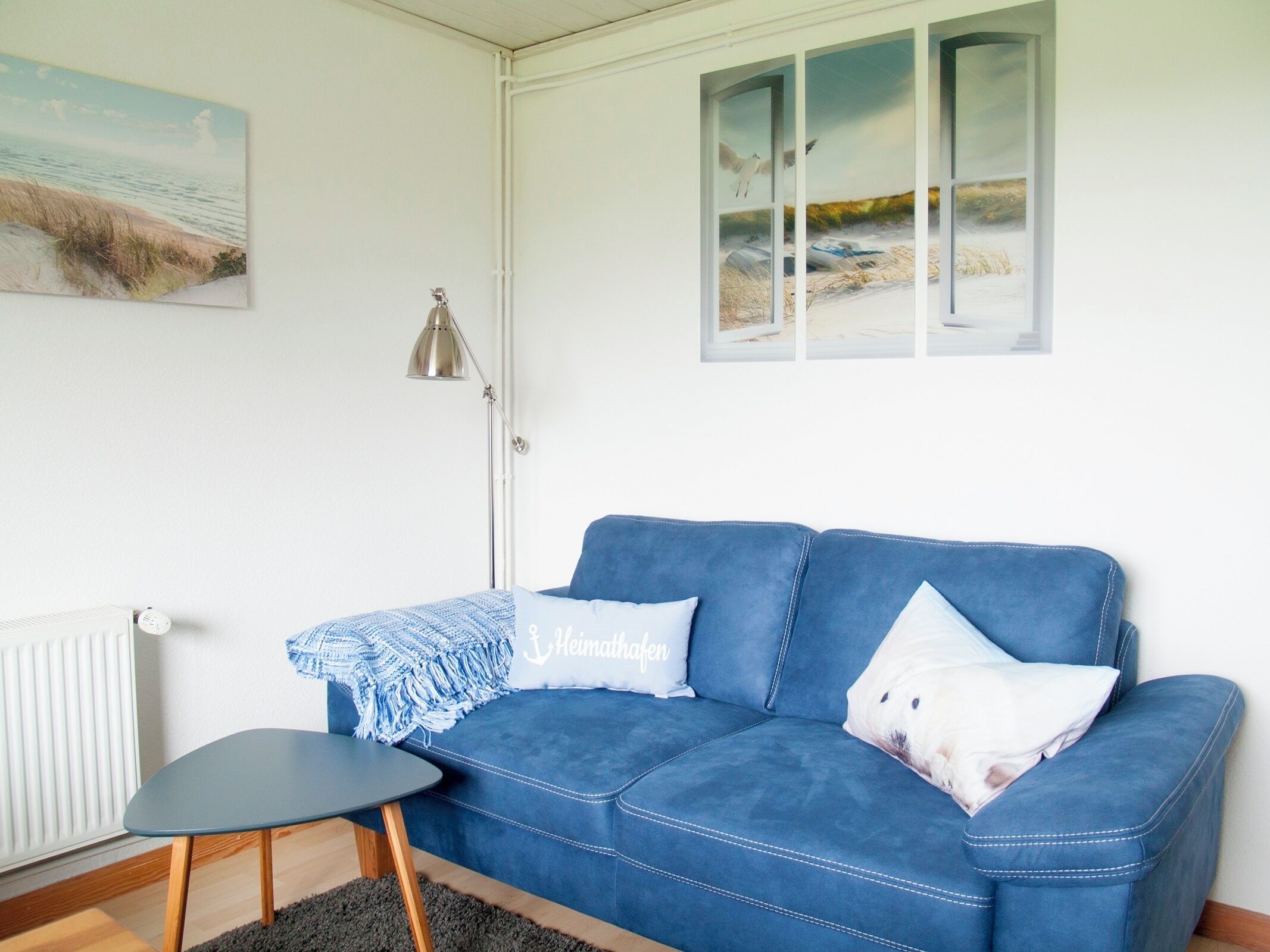 A room with a blue sofa, a small table, a lamp, and a painting on the wall.