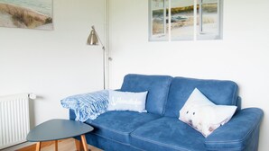 Een kamer met een blauwe bank, een bijzettafeltje, een lamp en een schilderij aan de muur.