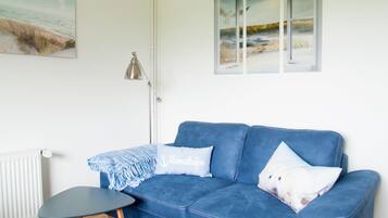 A room with a blue sofa, a small table, a lamp, and a painting on the wall.