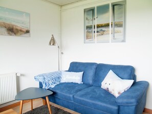 Ein Zimmer mit einem blauen Sofa, einem kleinen Tisch, einer Lampe und einem Bild an der Wand.