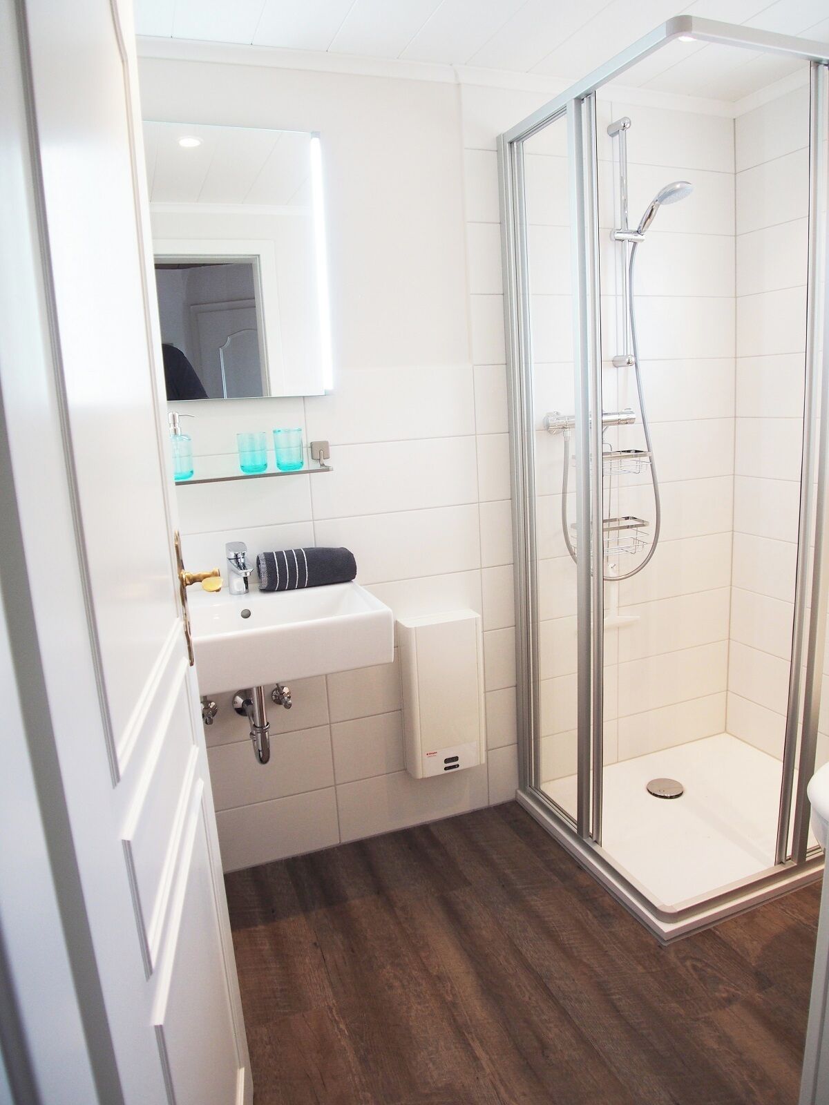 Ein modernes Badezimmer mit einer gläsernen Duschkabine, einem weißen Waschbecken mit Spiegel darüber und Holzboden.