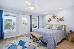 A bedroom with a bed, a bench, a ceiling fan, and a view of the outside. - High Tides & Good Vibes- Seacliffs-North Cape San Blas (Port St. Joe)