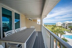 A balcony with a wooden table and chairs, overlooking a pool and beach. - High Tides & Good Vibes- Seacliffs-North Cape San Blas (Port St. Joe)