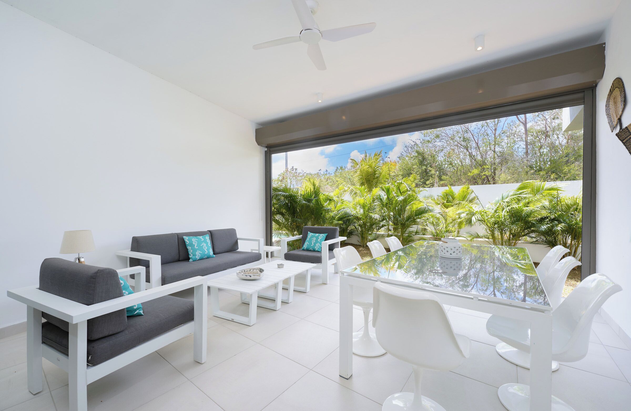 Un salón moderno con una mesa de vidrio, muebles blancos y vistas a espacios verdes.