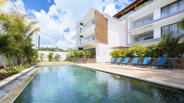 Um hotel moderno com piscina, espreguiçadeiras e um céu azul límpido.