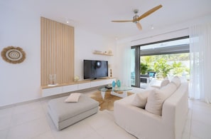 Ein modernes Wohnzimmer mit Flachbildfernseher, Deckenventilator, Glastisch und einer Couch.