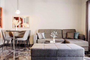 Una sala moderna con sofá, reposapiés, mesa de comedor, sillas y un florero con ramas decorativas.