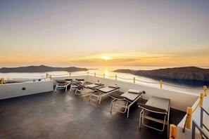 En solbeskinnet terrasse med liggestole og havudsigt i solnedgang.