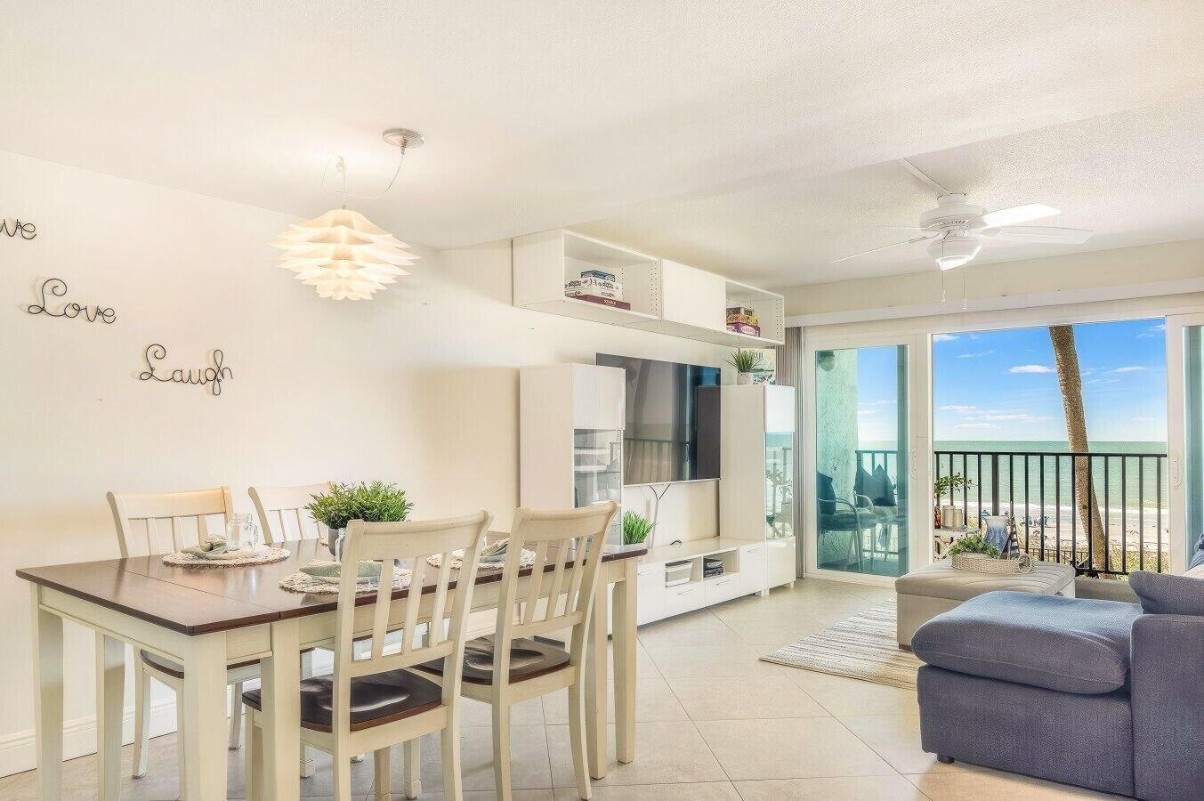 A modern living room with a dining area, a TV, and a balcony with a view of the beach.