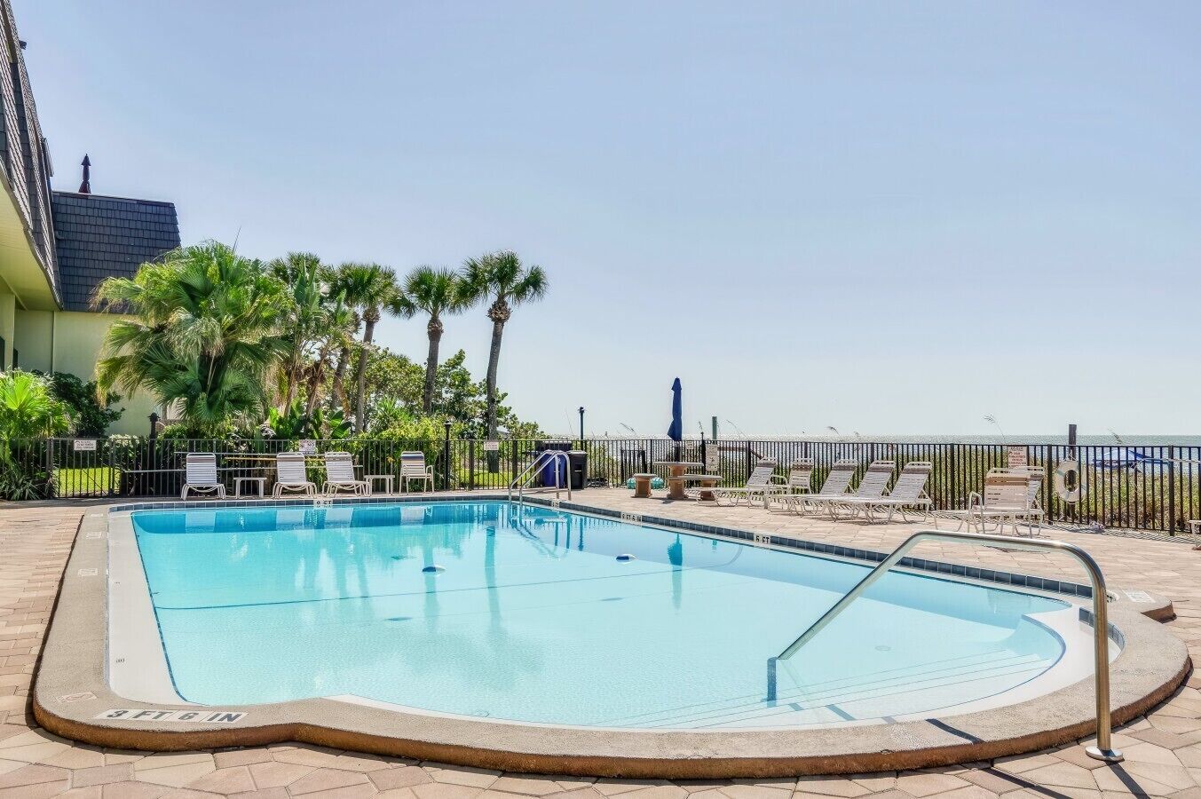 A swimming pool with lounge chairs, palm trees, and a view of the ocean.