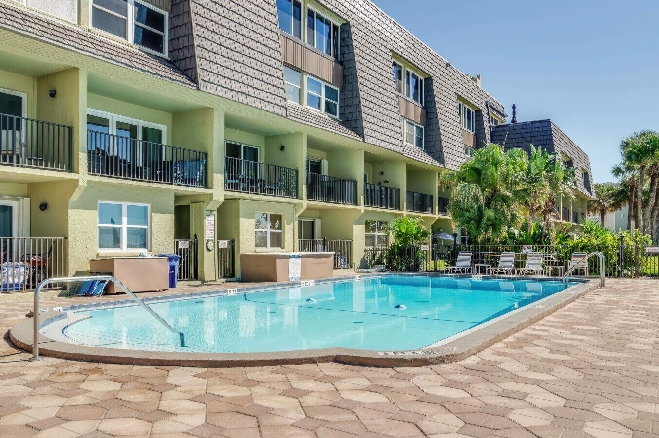 Ein mehrstöckiges Hotel mit Schwimmbad, Außenbereich und Palmen.