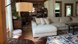 Ein gemütliches Wohnzimmer mit einem Ecksofa, einem Couchtisch und einem Bücherregal voller Bücher und Dekorationsobjekten.