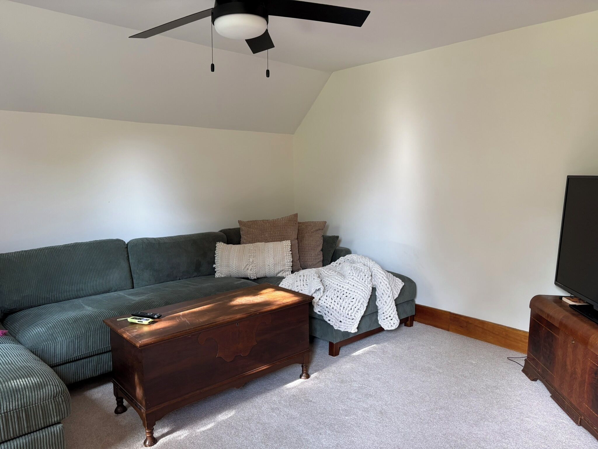 Un salon comprenant un canapé d’angle, une commode en bois, un téléviseur et un ventilateur de plafond.