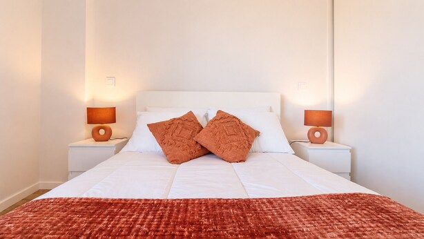 A neatly made bed with two pillows, white bedding, and two bedside lamps on white nightstands. - Vanguard View Apartment (Câmara de Lobos)