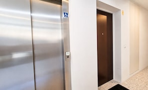 A modern elevator with a metallic finish and a blue accessibility sign. - Vanguard View Apartment (Câmara de Lobos)