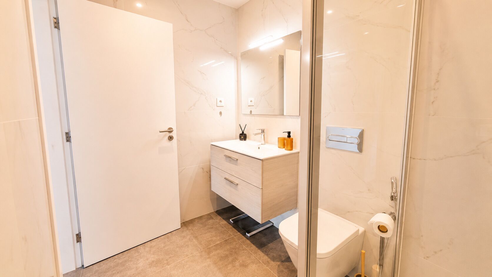 Un baño moderno con un inodoro blanco, un lavamanos con espejo y una zona de ducha.