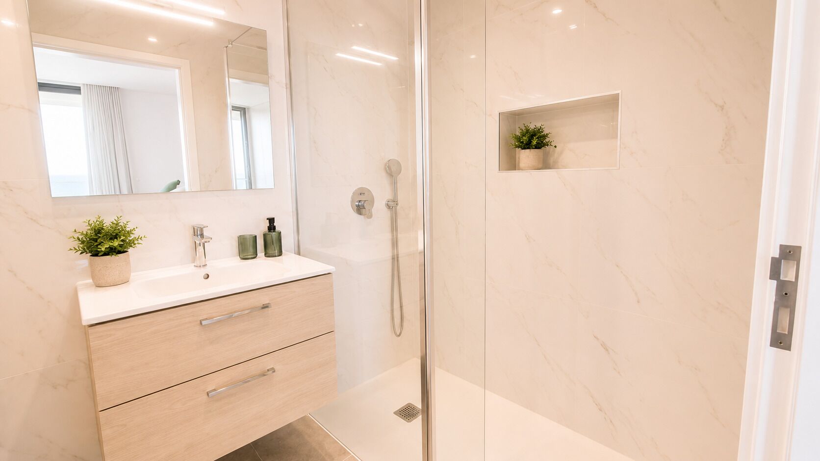 Un baño moderno con ducha de vidrio, tocador con espejo y un pequeño estante con una planta.