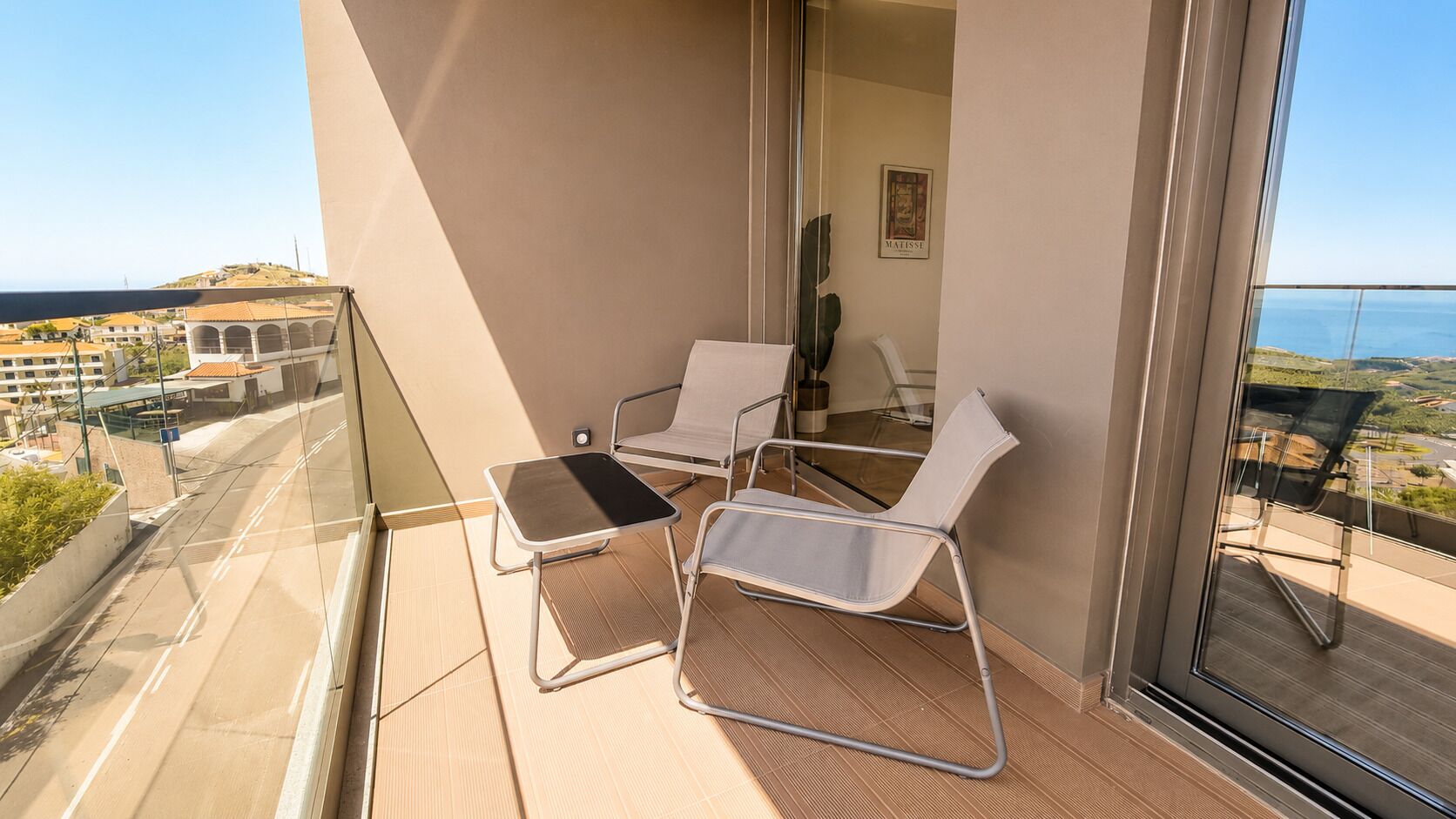 A balcony with two chairs and a small table, overlooking a cityscape.