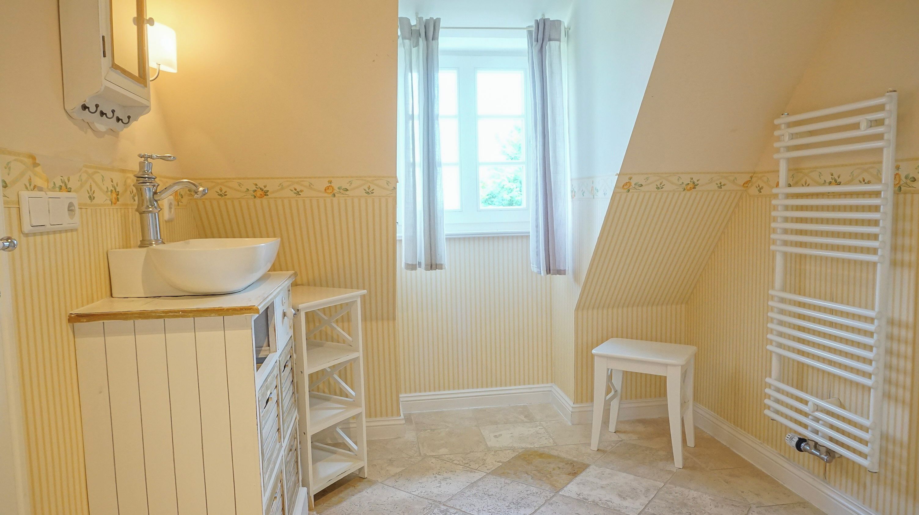 A bathroom with a vessel sink, a small stool, a radiator, and a window with curtains.