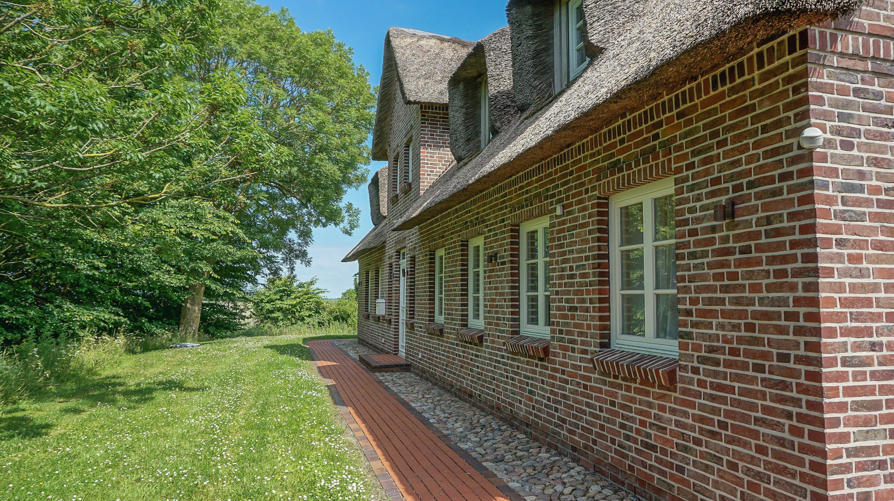 A brick building with a sloped roof, a pathway leading to the entrance, and a tree-lined background.