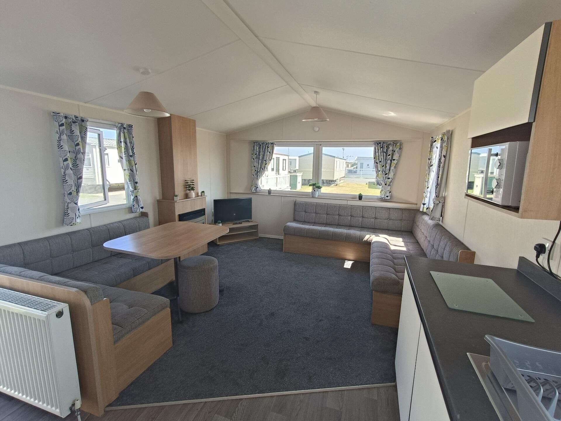 A modern RV interior with a dining area, seating, a TV, and a kitchenette.