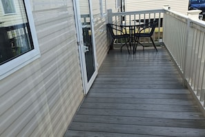 A wooden deck with a table and chairs, a sliding glass door, and a white railing. - Cozy 2 Bedroom Caravan Golden Sands (Rhyl)