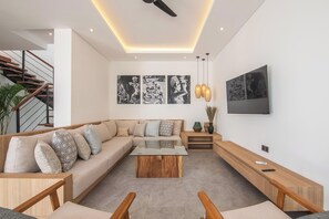 A modern living room with a sectional sofa, a glass coffee table, a wooden bench, a TV mounted on the wall, and a staircase with wooden railings. - Brand New 4br Villa, Close to nature (Canggu)