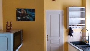A kitchen with a microwave, a white door, a clock, and a shelf with dishes.