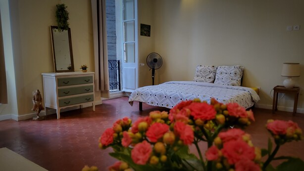 A bedroom with a bed, dresser, fan, and a window with a view.