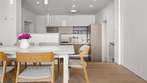 Een moderne keuken met witte kasten, een wit aanrechtblad en een eethoek met een witte tafel en houten stoelen.