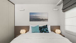 A hotel room with a bed, two bedside lamps, a wall-mounted picture, and a window with blinds. - Pedacito de Cielo 1 BDR Sew View apartment & pool (Zagorje)