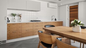 A modern kitchen with wooden cabinets, a white countertop, and a dining area with a wooden table and chairs. - Pedacito de Cielo 1 BDR Sew View apartment & pool (Zagorje)