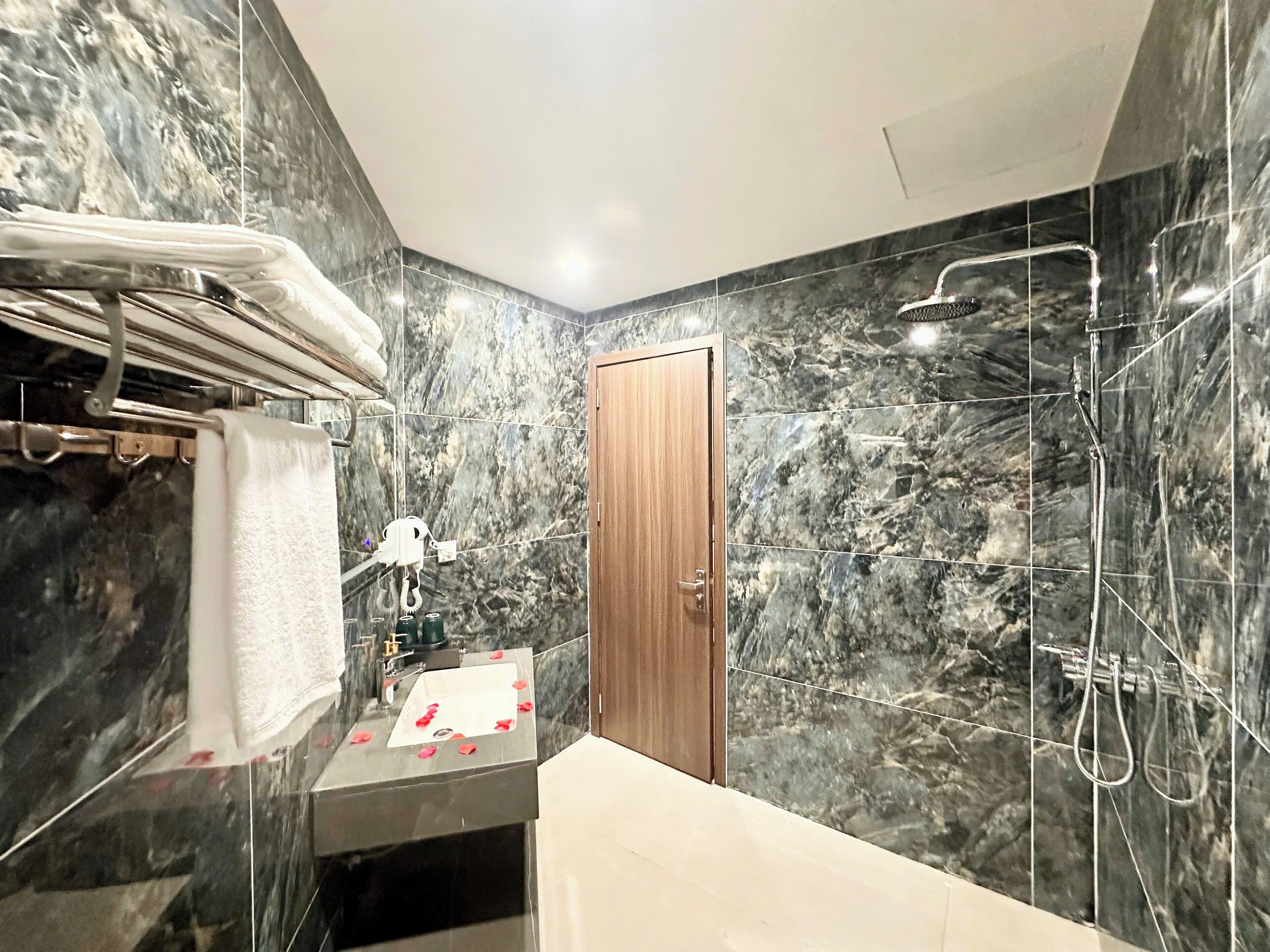 A modern bathroom with a marble wall, a wooden door, a shower, and a towel rack.
