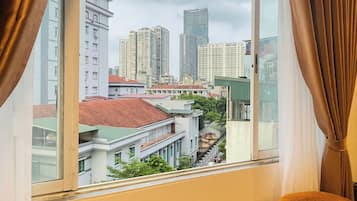 A room with a view of a cityscape through a large window, a table with a bottle and glasses, and two chairs.