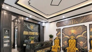 A reception area with a marble wall, two golden chairs, and a reception desk. - Vera Luxury Hotel (Hanoi)