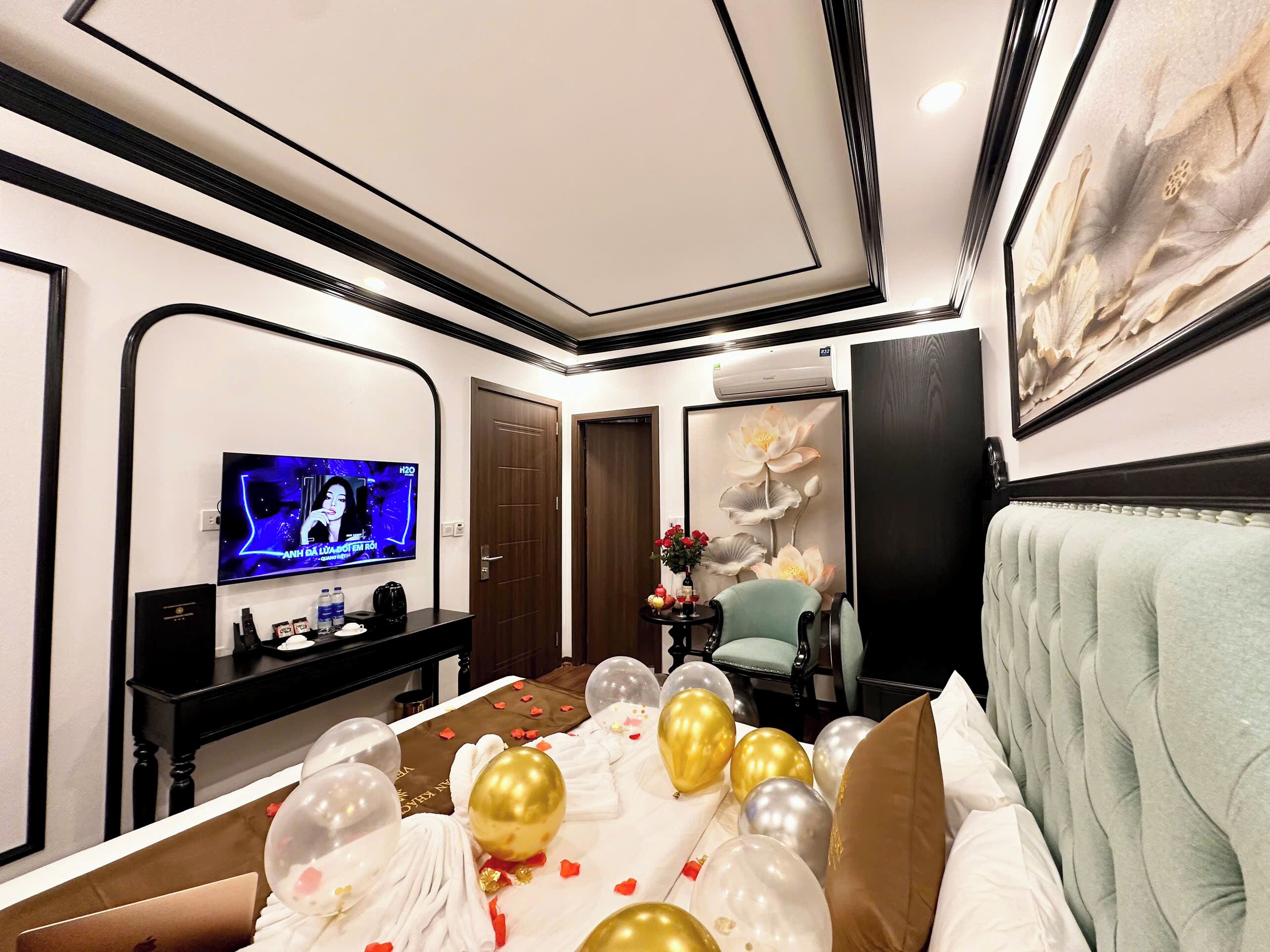 A hotel room with a bed, a TV, a desk, and a large floral painting.